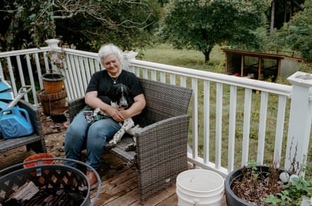 A woman and a dog sit on a chair on a porch.