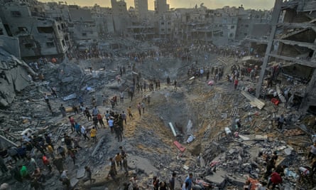 Crowds gather around a large crater in the ruined remains of the Jabalia refugee camp.
