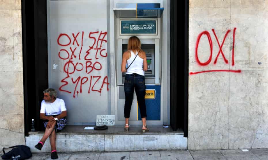 A woman withdraws money from an ATM machine in Thessaloniki, Greece next to a beggar and graffiti reading “no to fear”. 