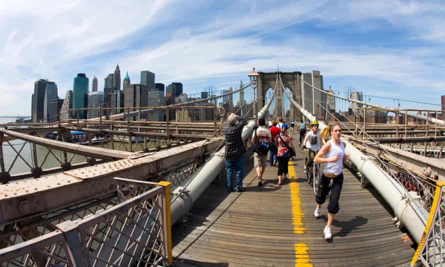 Brooklyn Bridge looking to Lower Manhattan downtown New York City with pedestrians and cyclists in sun sunshine with blue sky