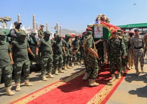 Soldiers in military fatigues and red berets carry a coffin along a path laid with a red carpet