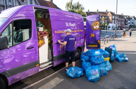 A purple van with the words 'St Raphael' on the side. There are blue bags filled with items on the pavement