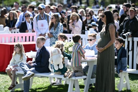 A pregnant woman holds her baby bump as children sit next to her on a picnic table