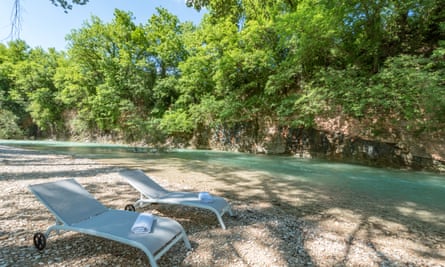 Sun loungers on the banks of a clear, turquoise river.