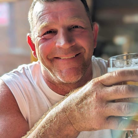 A man smiling at the camera holding a pint of beer