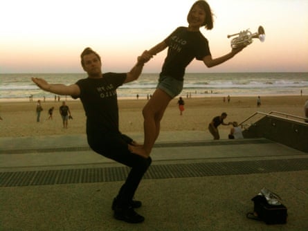 The couple in an acrobatic balance pose, with Sachie holding a trumpet