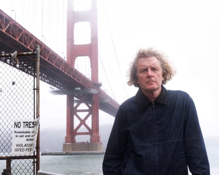 Grayson Perry wearing a black coat with Golden Gate Bridge in the background.