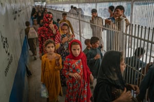 Women and children make their way along a narrow corridor between a wall and a white railing