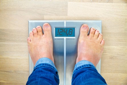A first-person view of a man standing on some digital scales showing his weight