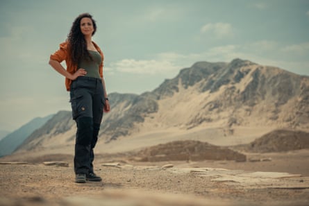 Ella Al-Shamahi poses with her hand on her hip in a desertscape, with mountains in the distance behind