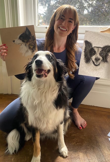 Daisy sits in front of her owner, who is crouching down and holding up two drawings of Daisy
