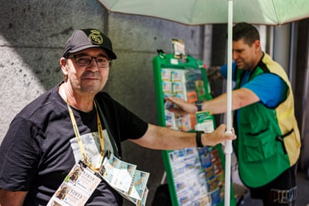 Ayuso, with lottery tickets on a lanyard around his neck, holds a parasol