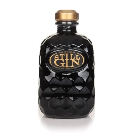 A bottle of Still G.I.N Gin. The bottle is black and deckled in a honeycomb pattern. There is a gold embossed label and a gold lid.