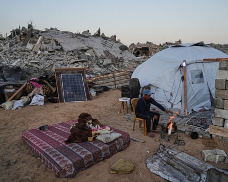 Displaced Palestinian Belal al-Yaziji sits by a fire outside his tent amid the destruction left by the Israeli air and ground offensive in Sheikh Radwan neighbourhood in Gaza City, Wednesday, 22 October 2025.