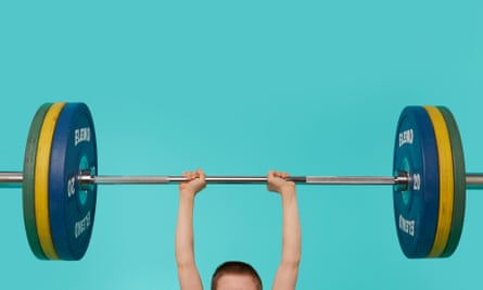 The top of a young boy's head and his arms holding a bar with heavy weights on