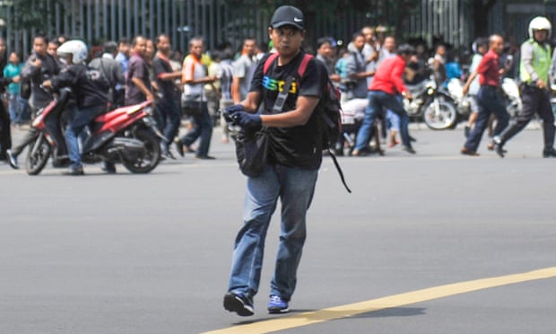 An unidentified man with a gun walks in the street as people run in the background on Thamrin Street near the Sarinah shopping mall in Jakarta
