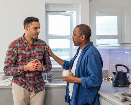Man in his 20s or 30s talking to an older man with a cup of tea in the kitchen