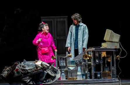 A woman in pink and a man in a long blue overcoat stand behind some old looking industrial hardware