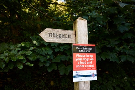 A waymarker for Tideswell village in the Peak District, with a sign attached asking that owners keep their dogs under control and leashed.