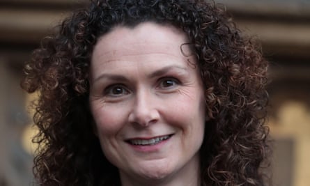 Wendy Chamberlain, with shoulder-length curly hair and wearing a round pendant on a chain, smiles