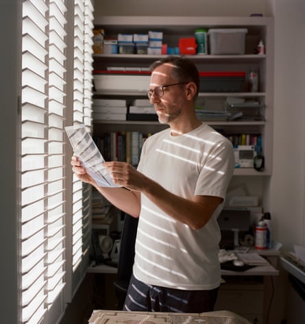 Writer David Batty standing in front of a window blind, looking at digital negatives made from Monti’s photographs