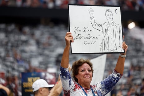 woman holds up poster with a drawing of charlie kirk and a bible verse