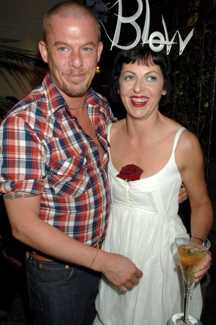 Alexander McQueen poses with his arm around the waist of Isabella Blow who is wearing a white headress of letters spelling Blow