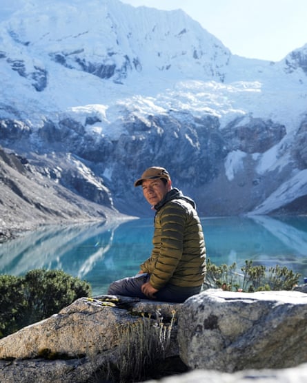 A man sitting on rocks facing a lake and snow-covered mountain.