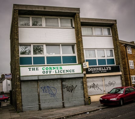 A graffiti-covered shuttered shopfront with the name Donelly’s above it sits next to a similar one named “The Corner Off-Licence”