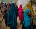 Women and children in colourful headscarves walk through a dusty displacement camp in Kismayo