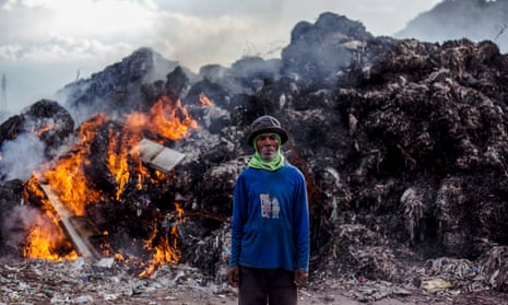 Indonesian scavanger Suparno, 60, stands in front of burning plastic waste at an imported plastic dumpsite in Mojokerto