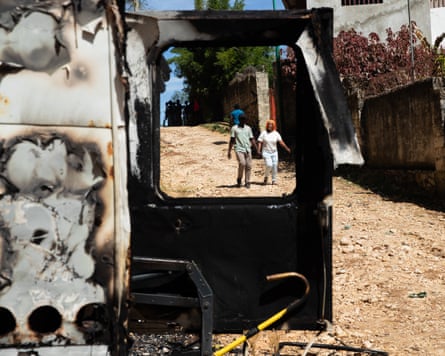 People walk past the remains of a vehicle after a night of violence in Kenscoff.