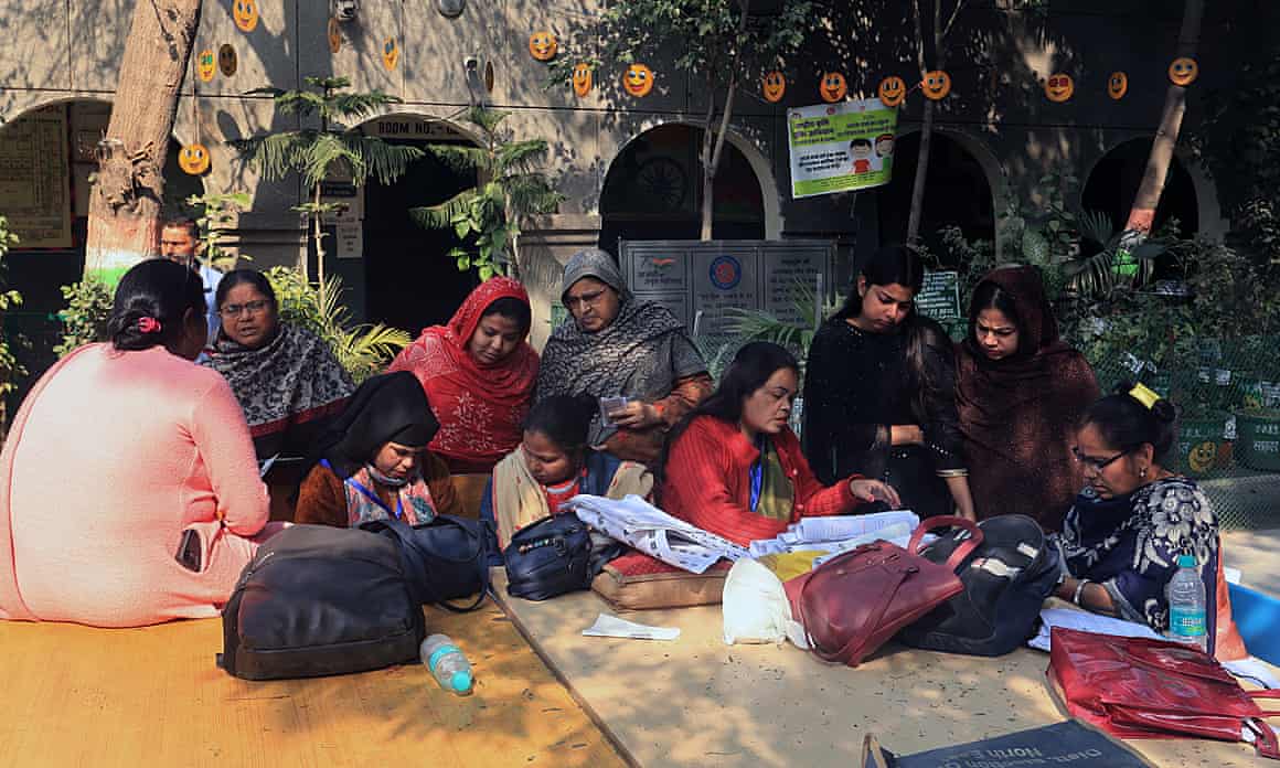 Voters check their names on voting lists outside a polling station in Delhi on 5 February