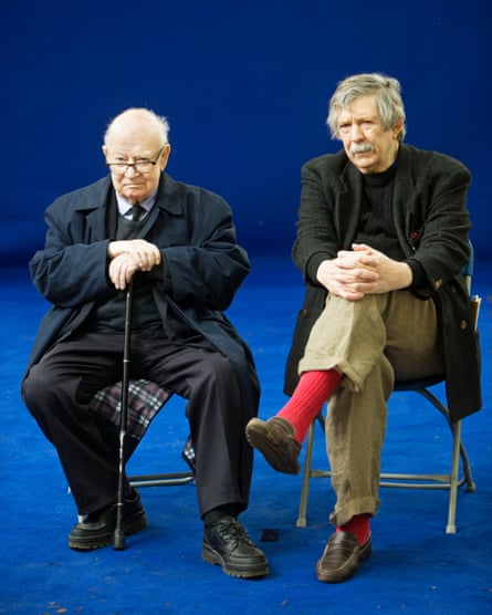 Jim Haynes and John Calder, who is holding a walking stick sitting on chairs on a blue stage