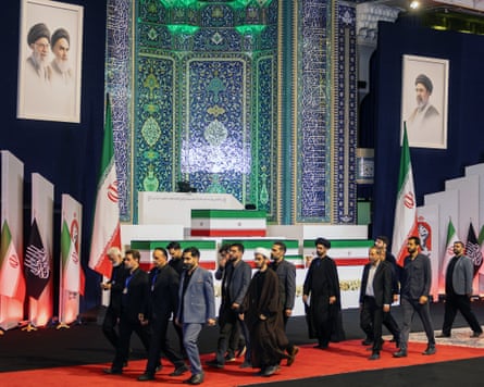 Officials walk past the coffins which are arranged on different levels of a stepped structure on a stage