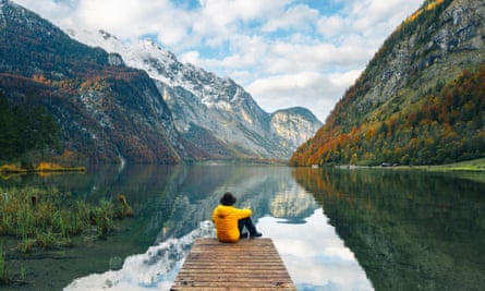 One man sitting on a boat pier admiring the Konigssee lake, Bavaria, GermanyGettyImages-1282659148