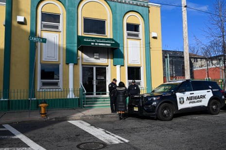 two police officers speak to a woman next to a police car outside a green and yellow building