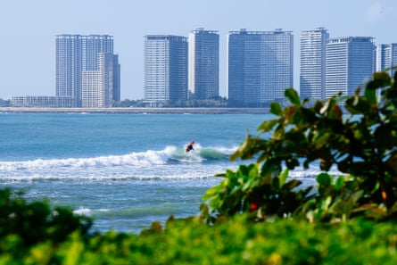 A view over some trees of a surfer competing in the Wanning International on Hainan Island, China, with tall buildings in the background on the other side of the bay
