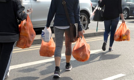 Shoppers carrying plastic bags across a supermarket car park