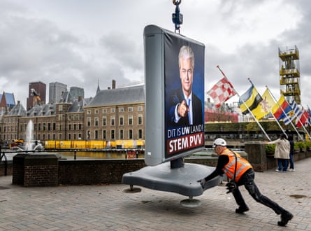 An employee installs an election sign showing Geert Wilders in a street with flags nearby