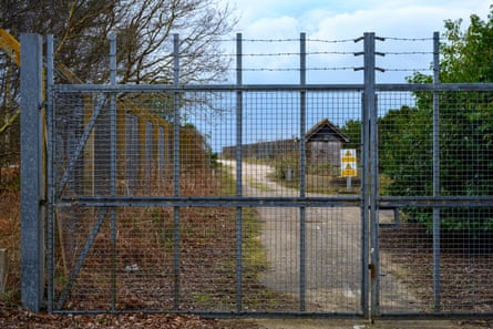 A large metal fence with barbed wire prohibits access to a path in the forest