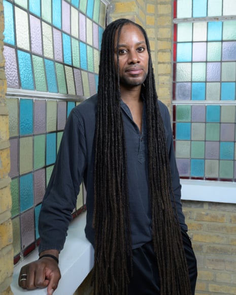 Jason Arday wearing a dark shirt stands in front of colorful stained glass windows