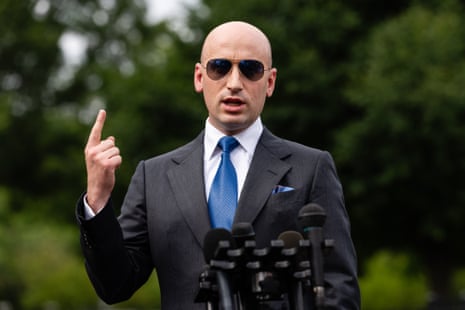 Stephen Miller, in sunglasses and a suit, gestures while speaking into microphones outdoors