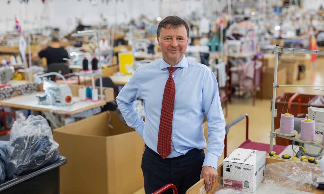 Christopher Nieper stands next to large spools of thread. Factory in soft focus behind him