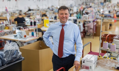 Christopher Nieper stands next to large spools of thread. Factory in soft focus behind him