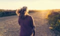 Rear view of woman walking on dirt road during sunset