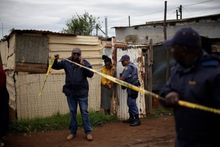 A police officer holds up police tape on a muddy street next to ramshackle buildings
