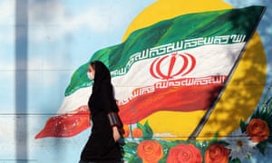 A woman wearing a face mask walks past a mural of Iran’s national flag in Tehran.