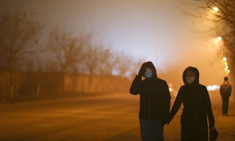 People walk down a street wearing masks on a heavy pollution evening in Beijing, China