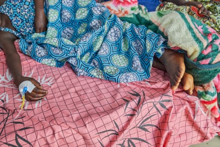 A woman, whose face is out of shot, lies on a bed with a stent in her hand.